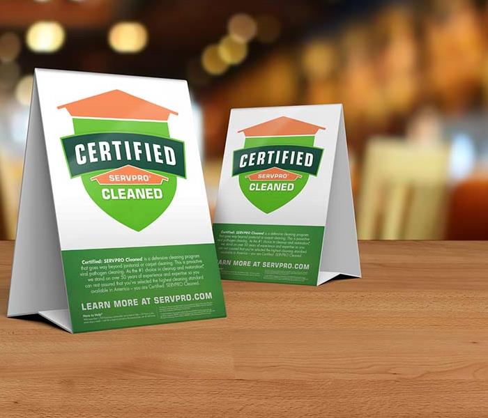 Table tent signs describing the Certified: SERVPRO Cleaned program on top of a wooden table